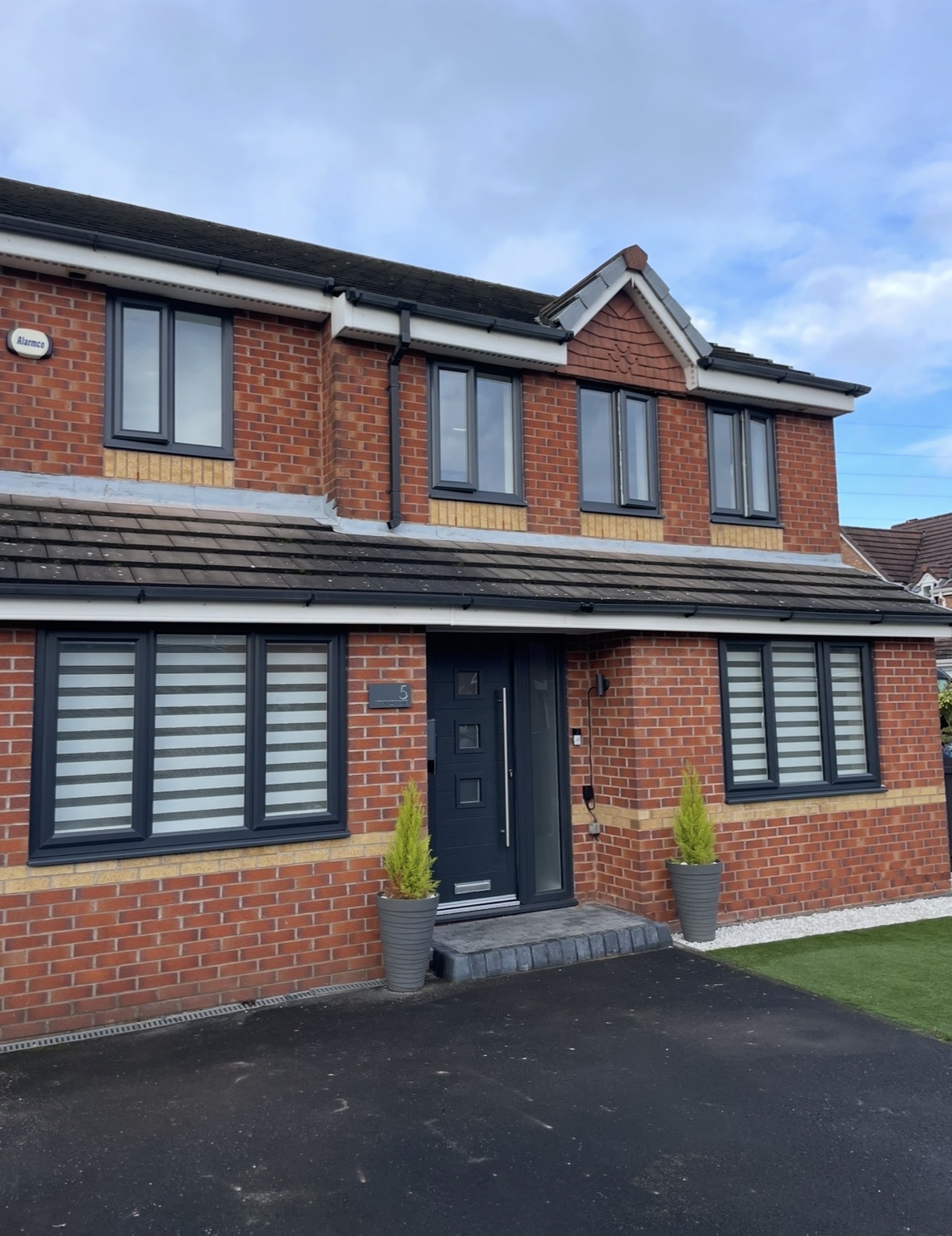 Red brick home with newly installed anthracite windows and composite front door